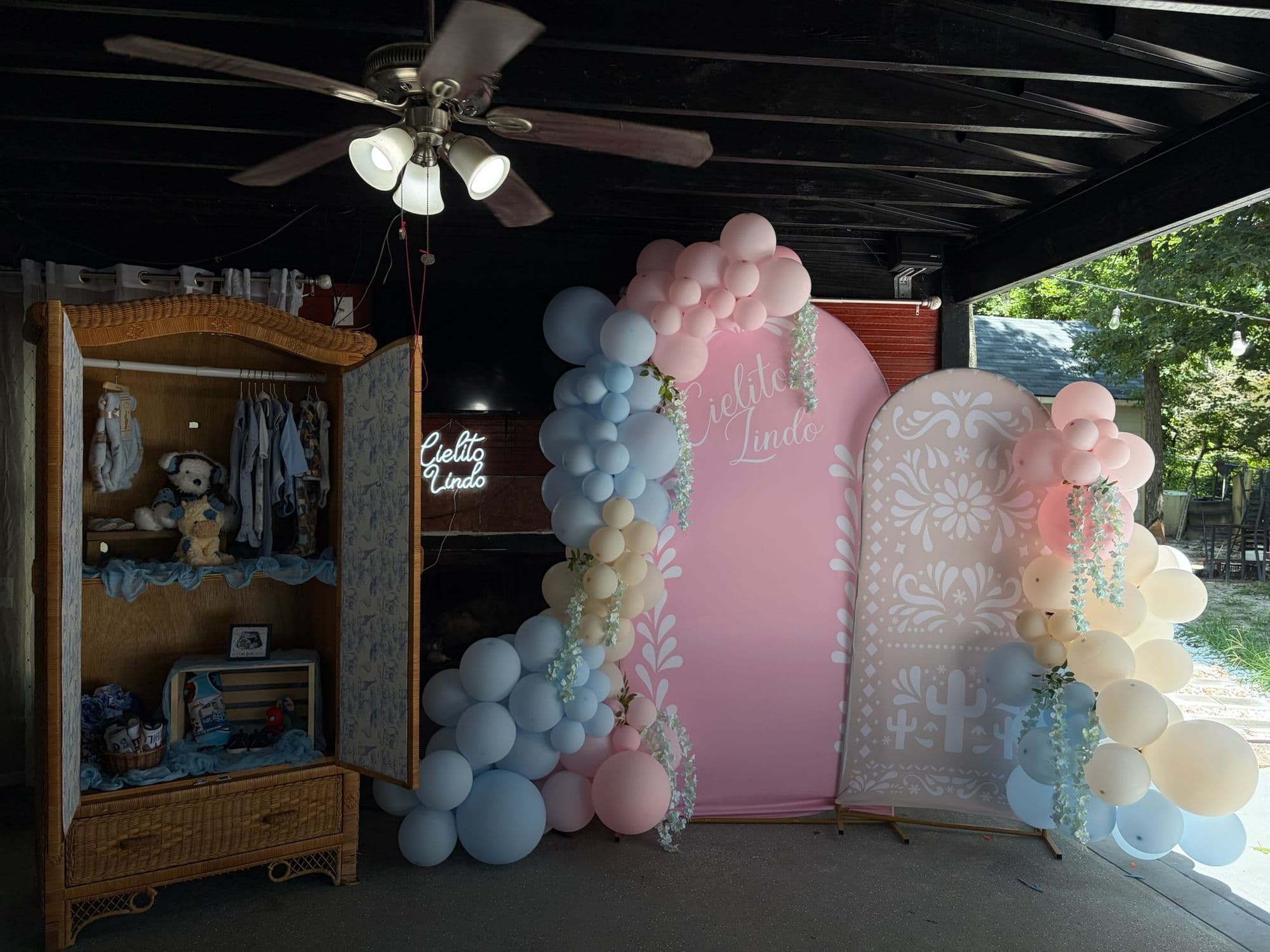 Ropero de mimbre, letrero de neón Cielito Lindo y guirnalda de globos rosa y azul sobre paneles en arco