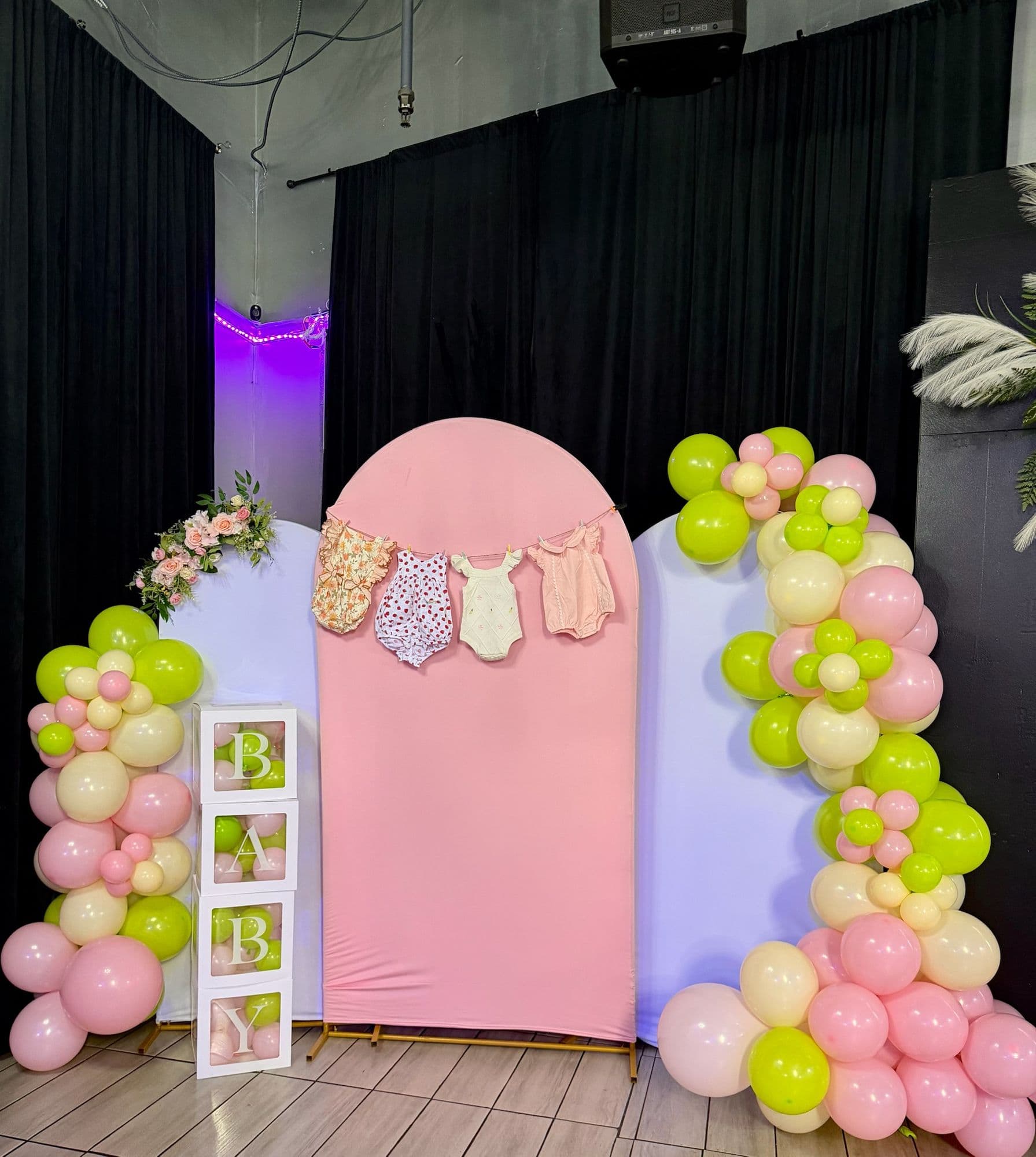 Fondo de arcos rosa y blanco con tendedero de ropita, bloques BABY y guirnalda de globos rosa, crema y verde lima
