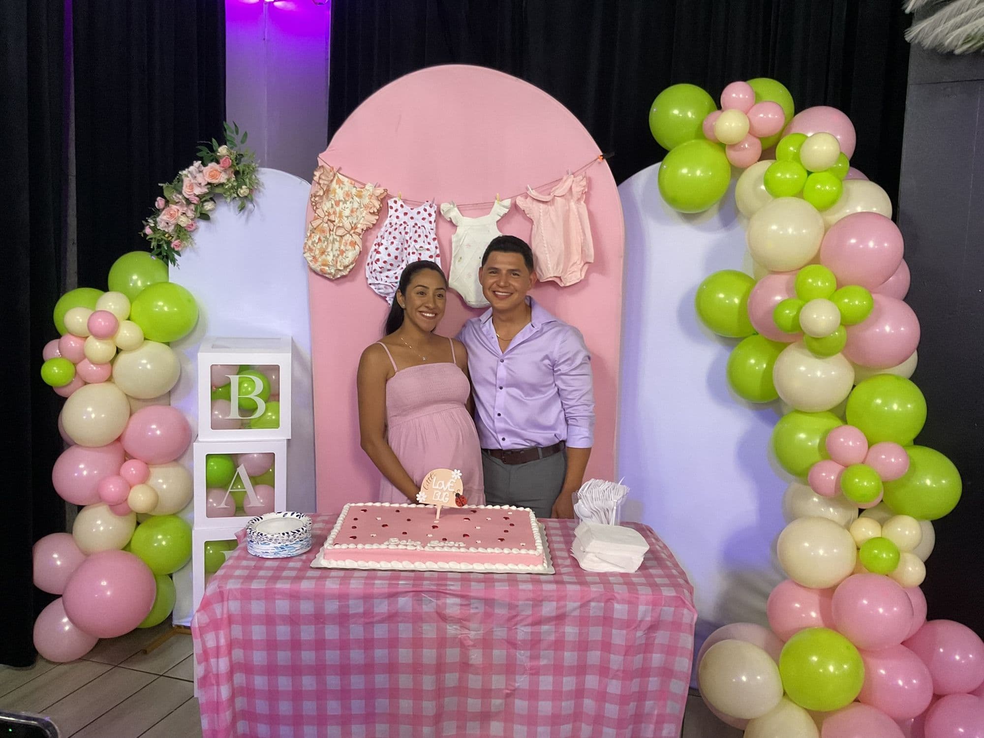 Los futuros papás frente al fondo detrás de la mesa del pastel en cuadros rosas
