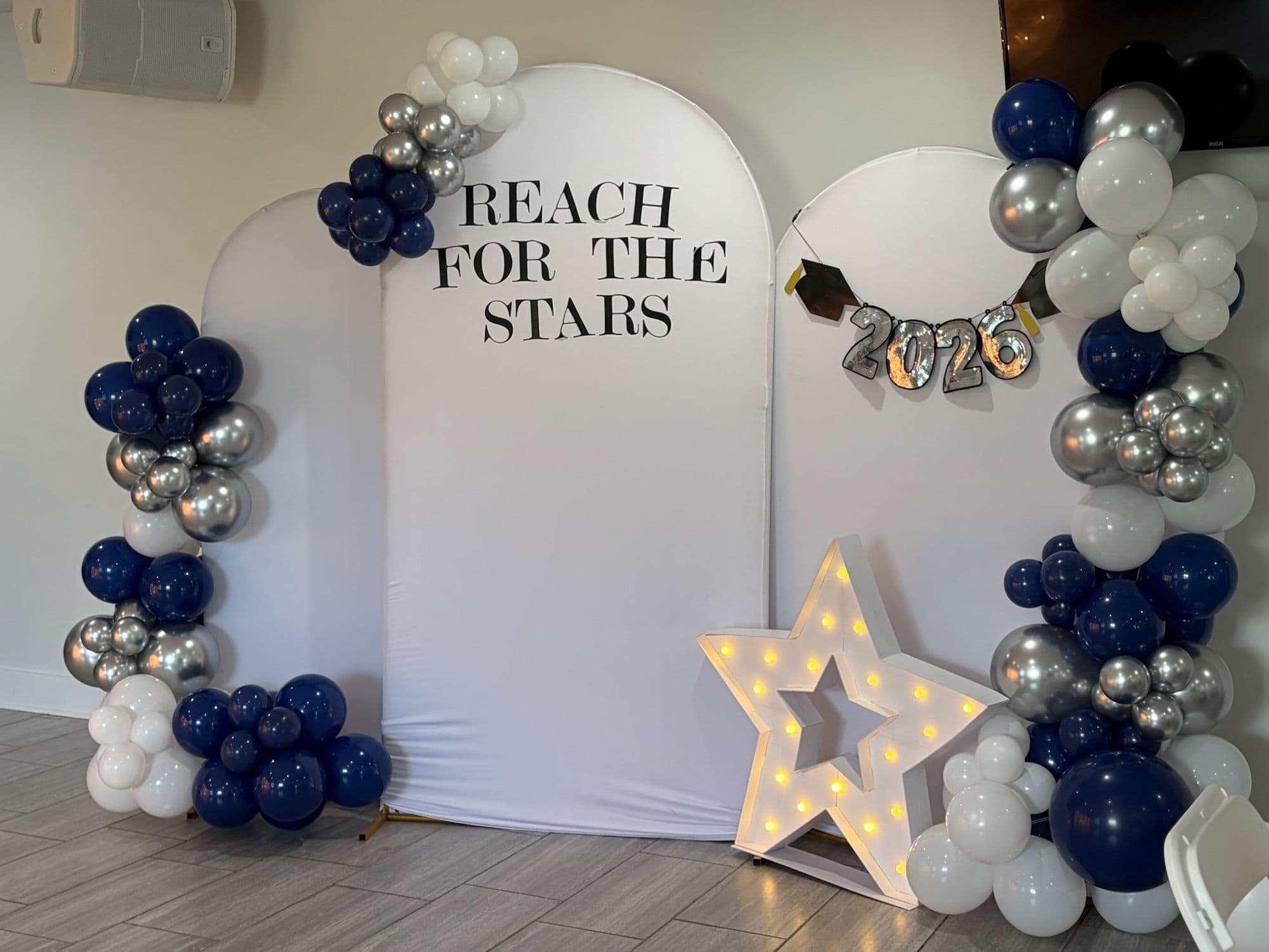 Reach for the Stars arch backdrop with navy, silver, and white balloons and a lit star