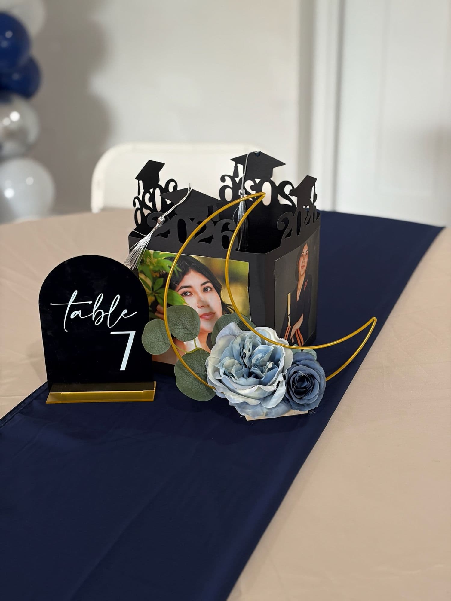 Graduation centerpiece with a gold moon, photo box, and blue florals