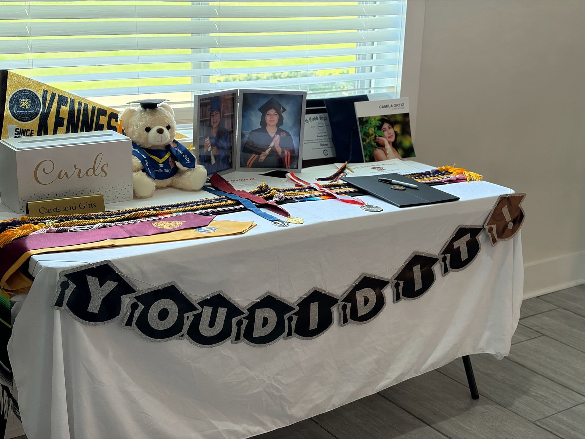 Memory table with a You Did It banner, stoles, photos, and a graduation bear