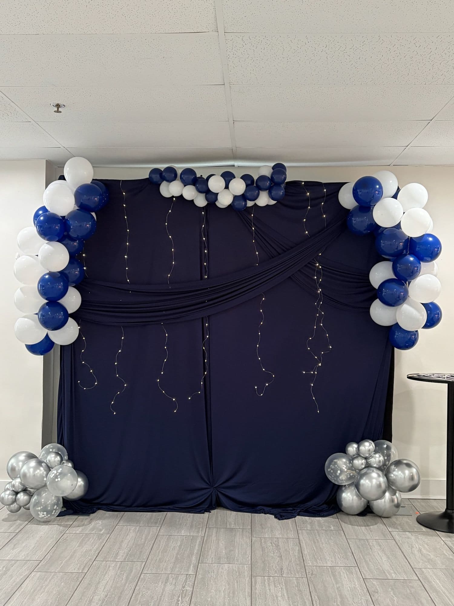 Navy draped photo backdrop with string lights and balloon accents