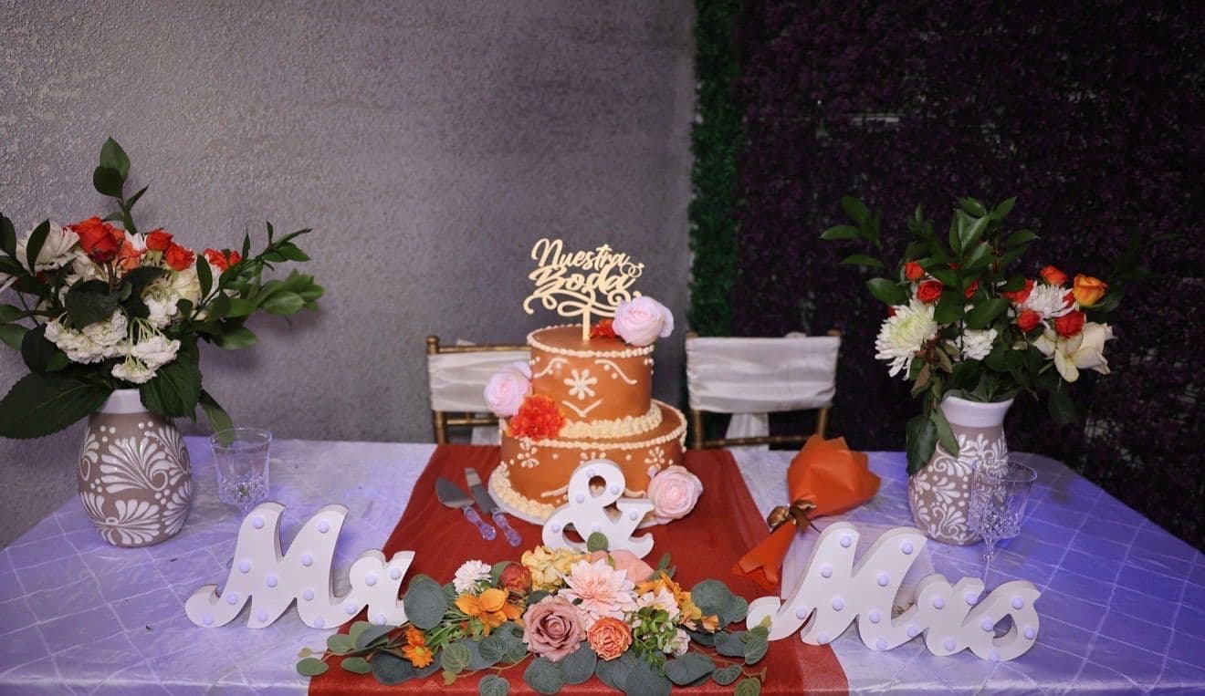 Terracotta wedding cake with a Nuestra Boda topper between floral arrangements