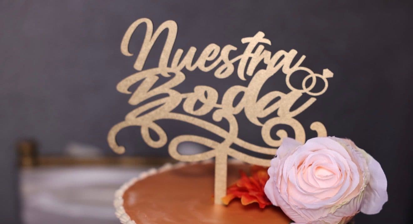 Close-up of the gold Nuestra Boda cake topper and a blush rose