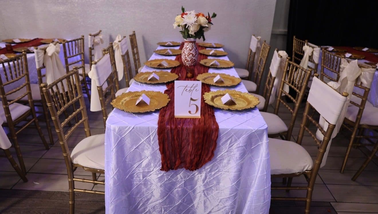Long guest table with gold chairs, white sashes, and a terracotta runner