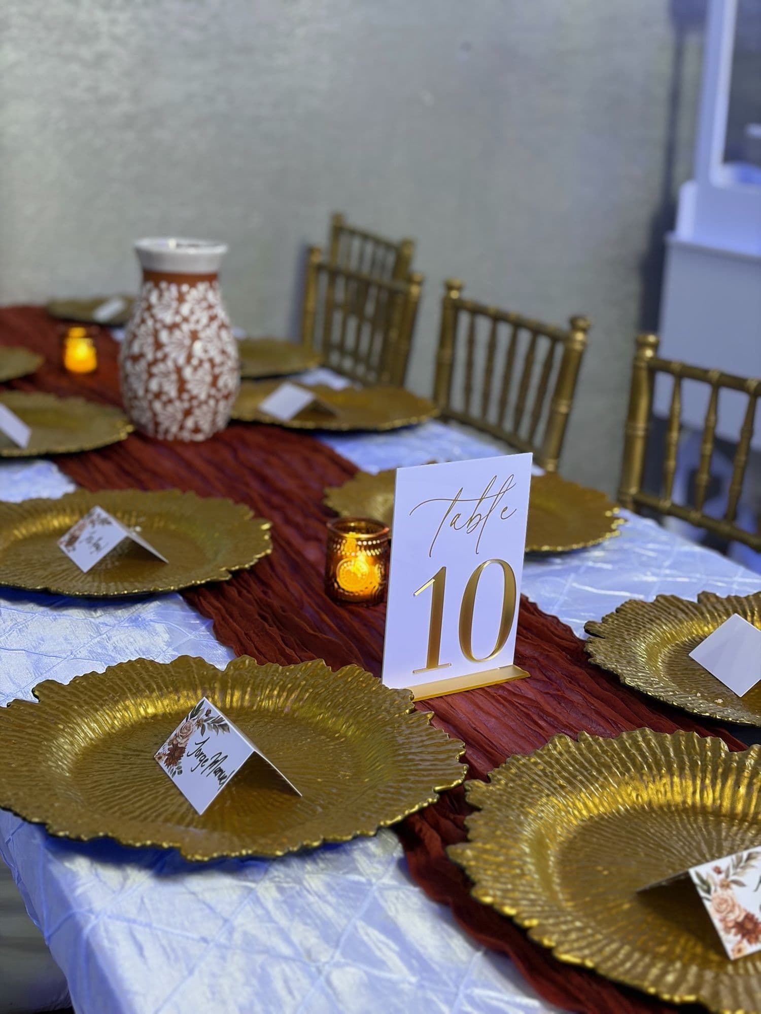 Gold chargers, terracotta runner, and table number 10 with a hand-painted vase