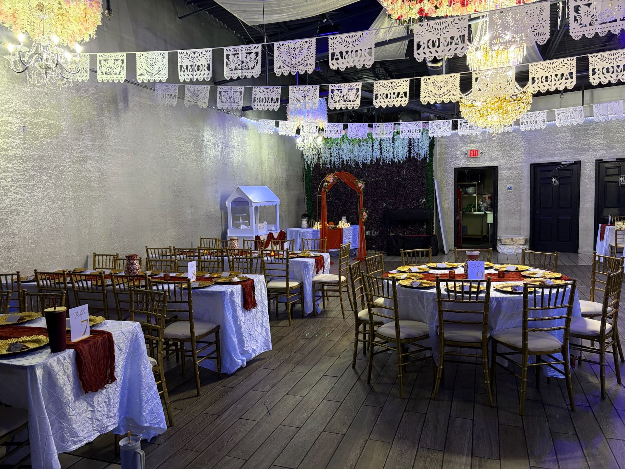 Reception hall with papel picado banners, white linens, terracotta runners, and gold chargers