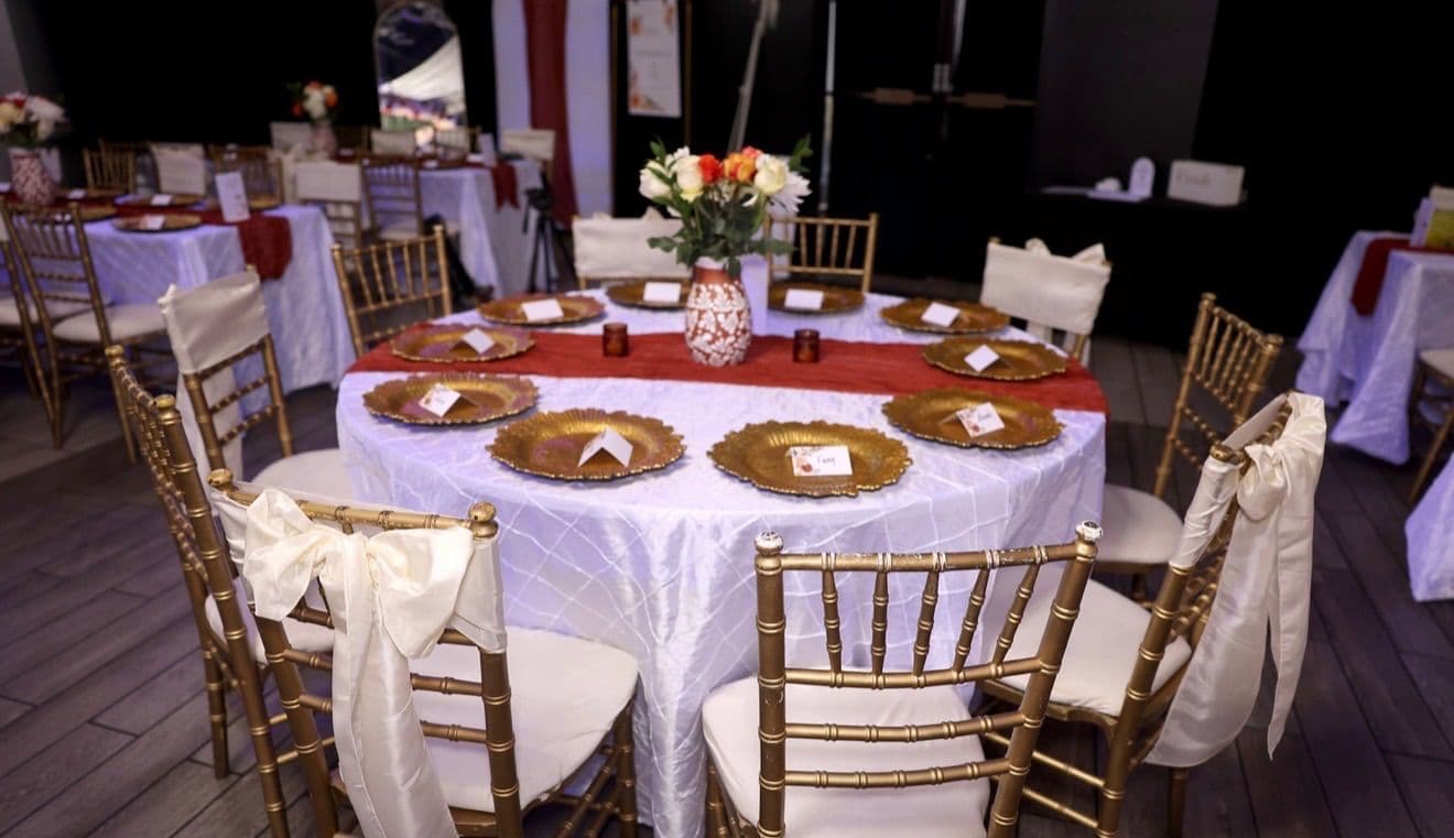 Round guest table with white linen, gold chargers, and a floral centerpiece