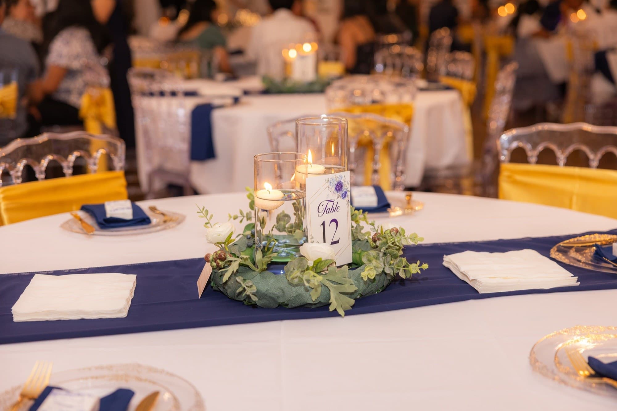 Floating-candle centerpiece with greenery and a navy table number