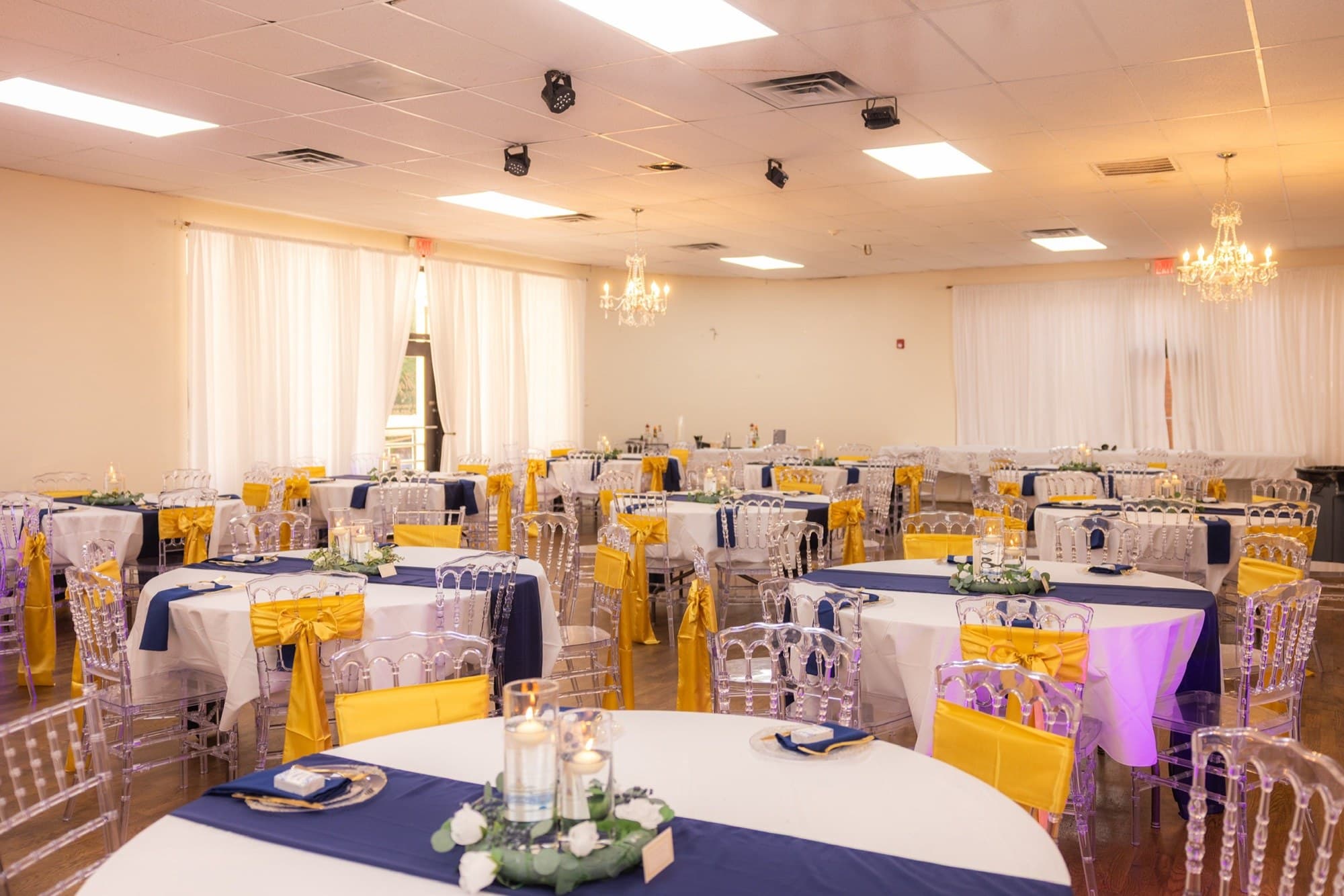 Reception hall with navy linens, gold sashes, and crystal chairs