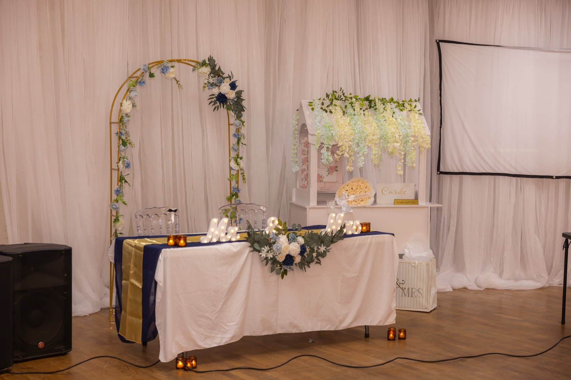 Sweetheart table beneath a gold floral arch with a card house